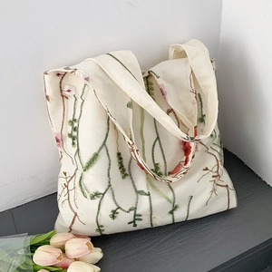 Close-up of floral embroidery detail on cream canvas tote bag with green leaves
