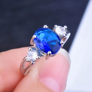 Close-up of a silver ring featuring a large oval blue sapphire and clear side stones