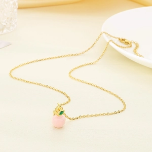 Minimalist gold necklace featuring a cute pink enamel apple pendant on a textured background