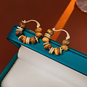 Macro shot of tiger eye stone earrings on a dark teal box with warm lighting