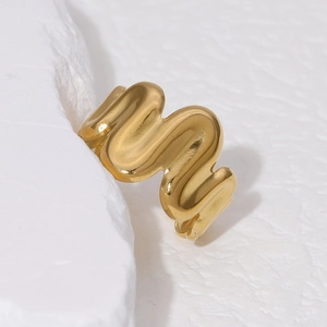 Irregular 18K gold plated stainless steel wave ring on a white textured stone base