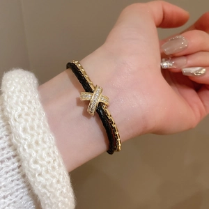 Détail d'un bracelet double couche avec breloque X dorée sertie de diamants sur poignet