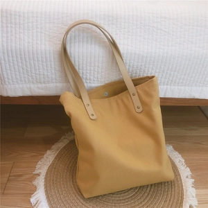 Detail view of yellow canvas tote bag with leather handles and magnetic snap closure