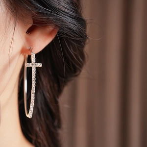 Dettaglio di modella che indossa orecchini a cerchio d'argento con croce di strass lucidi