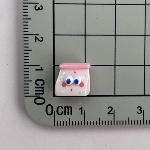 Close-up of mini pink resin cartoon charm next to a ruler showing its 1cm small size