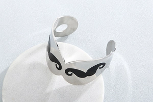 Detail of silver stainless steel open bangle featuring a black mustache design on stones
