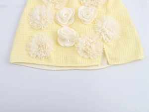 Dettaglio dell'orlo della gonna in tweed giallo con fiori 3D bianchi e spacco laterale