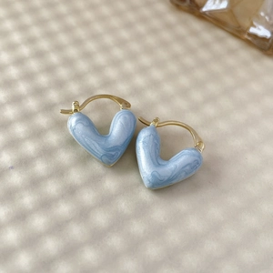 Vue détaillée de boucles d'oreilles cœur dorées avec une texture en émail marbré bleu clair