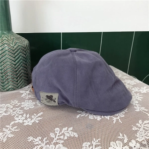 Detail of a purple-grey cotton beret cap with side label on white lace surface
