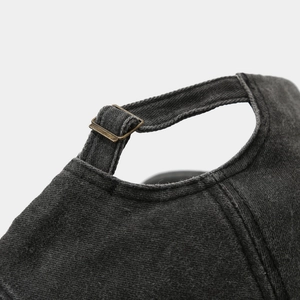 Detail of adjustable brass buckle on a black washed cotton baseball cap with fabric texture