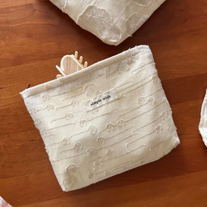 Detail of off-white cotton pouch showing textured jacquard fabric and simple wish label