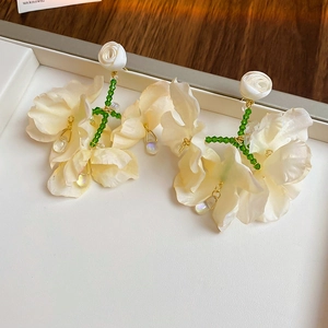 Detail of cream fabric flower earrings with green beads and silk rose on white tray