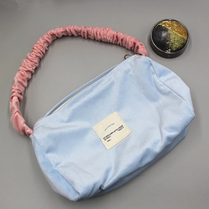 Detail of light blue corduroy shoulder bag featuring a pink ruffled handle and cloth label