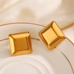 Polished gold square cushion earrings on white dish with elegant silk background