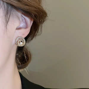 Detail eines eleganten goldenen Spiralohrrings mit weißer Perle und Kristallen