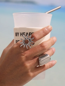 Detailed view of sun-shaped ring and wide gold band on a hand against beach background
