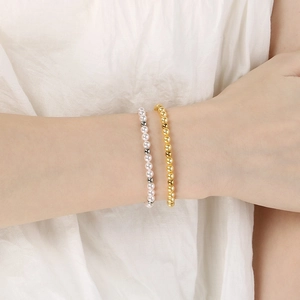 Detail of layered white imitation pearl bracelet and gold bead bracelet on a model wrist