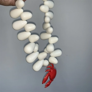 Detail of hand holding a sea style necklace with white beads and a red crab pendant