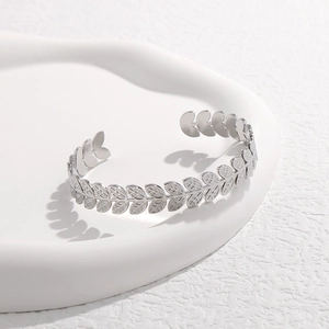 Primer plano del brazalete plateado con motivo de hojas en una bandeja de cerámica