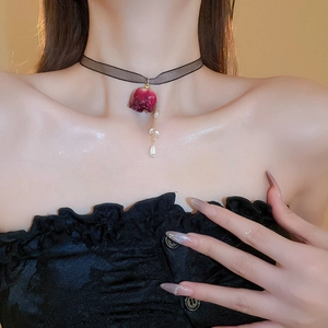 Nahaufnahme von schwarzem Spitzen-Choker mit roter Rose und Perlenquaste am Hals