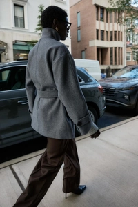 Street style view of grey wool coat with waist belt and standing collar design
