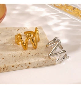 Detail of gold and silver irregular wave rings on a textured beige stone background