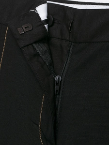 Detail of black trousers featuring a metal zipper, hidden hook closure and yellow stitching