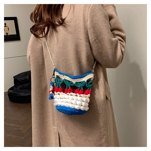 Detail of crochet bucket bag with 3D cherry pattern and pearl chain strap on camel coat