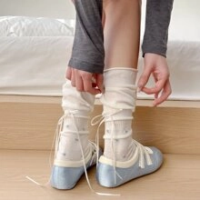 Detail of cream slouch socks with ribbon ties paired with blue ballet flats in a soft room