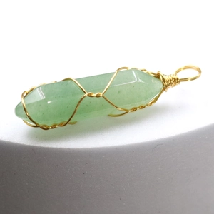 Macro view of green hexagonal crystal pendant with gold wire wrap on white background