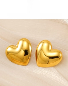 Close-up of polished 18k gold heart-shaped stud earrings on a soft silk fabric background
