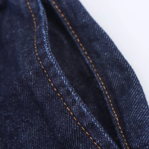 Gros plan des coutures jaunes sur la poche en denim bleu foncé à texture sergé