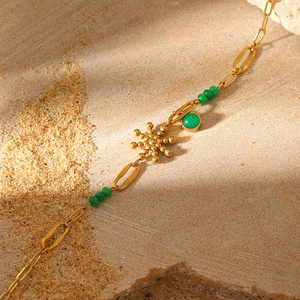 Detail of gold chain bracelet with green beads, sun starburst and round green stone pendants
