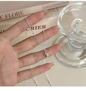 Close-up of S925 sterling silver heart necklace held by hand over a minimalist background