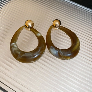 Detail of brown marble resin teardrop earrings with gold ball studs on textured glass
