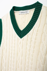 Detail of V-neckline with green contrast trim and cable knit texture on cream vest