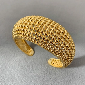 Detail eines offenen Armreifs mit goldenem Perlengeflecht auf grauem Filzhintergrund