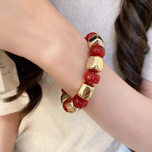Close-up of red glitter beads and golden geometric blocks on an acrylic stretch bracelet