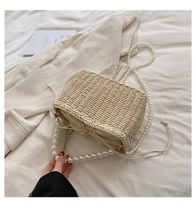 Detail of straw woven bag with pearl chain strap and drawstring closure on a bed