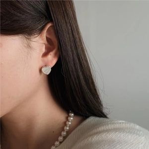 Close-up of minimalist heart stud earrings with a pearl necklace and white knit sweater