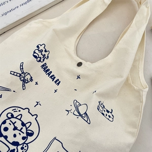Detail of canvas tote bag showing blue cartoon astronaut print and metal snap button closure