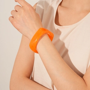 Close-up of a wide bright orange resin cuff bracelet on a model's wrist with minimalist style