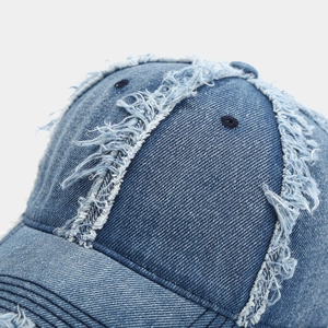 Detailed view of distressed frayed edges and texture on deep blue denim baseball cap