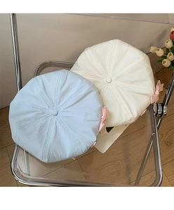 Detail of corduroy beret hats in light blue and beige with checkered bow on a chair