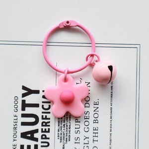 Detailed view of a pink knit flower and bell keychain on a minimalist white display card