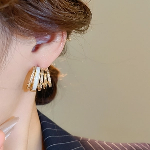 Close-up of gold plated C-shaped earrings with zircon inlay and white enamel detail