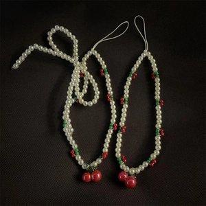 Close-up of beaded phone charms featuring white pearls, green beads, and red cherry charms