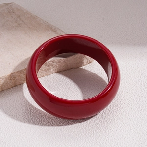 Detail of a chunky red resin bangle with a glossy finish on a textured background