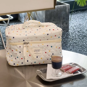 Detailed close-up of quilted polka dot makeup bag with ribbon zippers on a cafe table