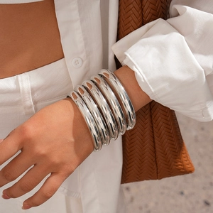 Close-up of six chunky silver metallic bangles stacked on a wrist with polished finish